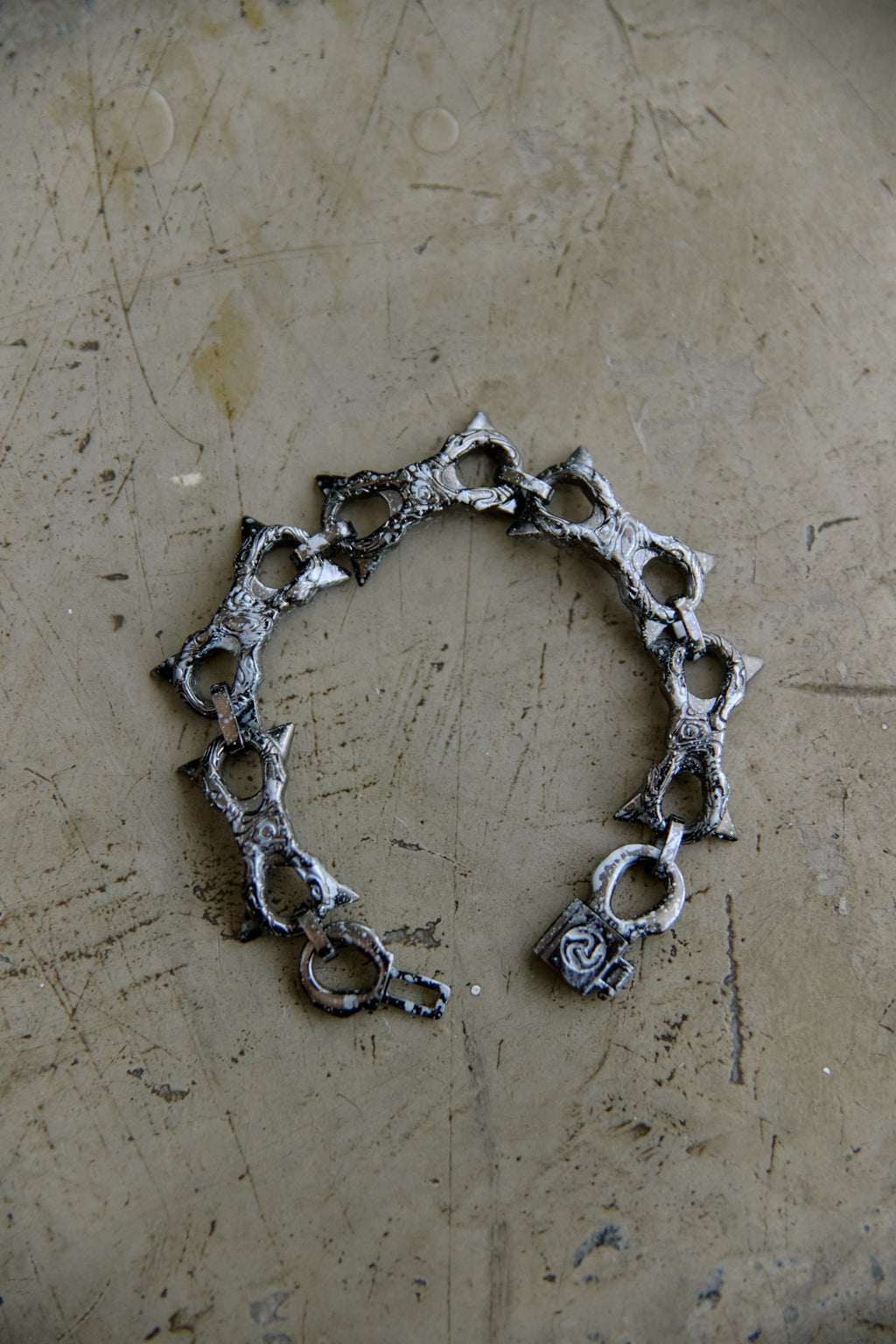 A handmade silver-toned chain bracelet with textured, hammered details and openwork links, displayed on a scratched, metallic beige surface.