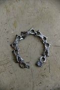 A handmade silver-toned chain bracelet with textured, hammered details and openwork links, displayed on a scratched, metallic beige surface.