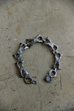 A handmade silver-toned chain bracelet with textured, hammered details and openwork links, displayed on a scratched, metallic beige surface.