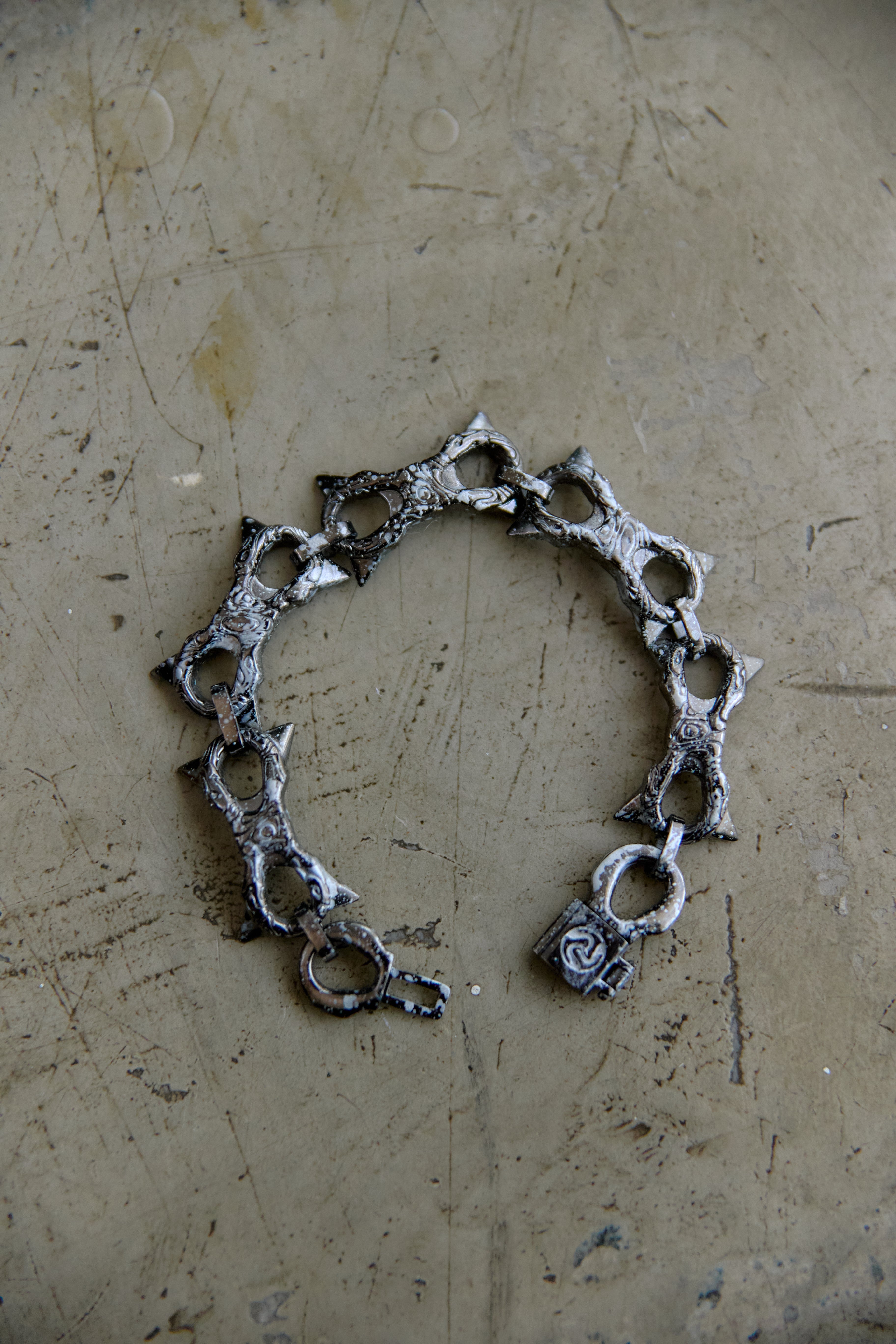 A handmade silver-toned chain bracelet with textured, hammered details and openwork links, displayed on a scratched, metallic beige surface.