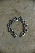 A silver-toned chain bracelet with star-shaped charms and small pink gemstone accents, displayed on a textured beige surface.