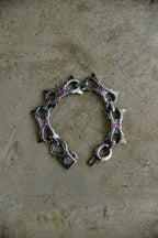 A silver-toned chain bracelet with star-shaped charms and small pink gemstone accents, displayed on a textured beige surface.
