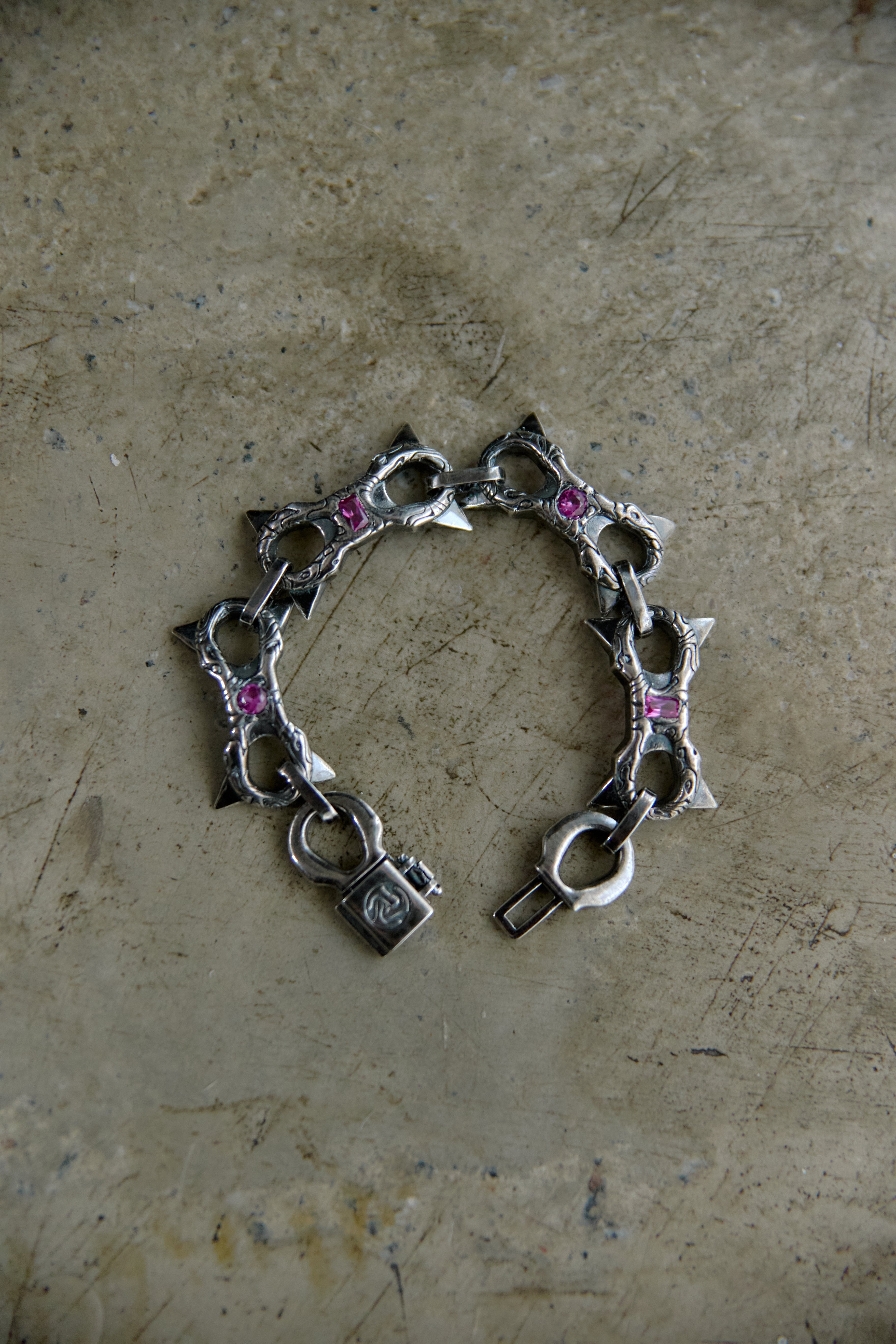 A silver-toned chain bracelet with star-shaped charms and small pink gemstone accents, displayed on a textured beige surface.