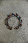 A handmade link bracelet with a padlock clasp, featuring a distressed copper and turquoise patina finish, displayed on a textured concrete surface.