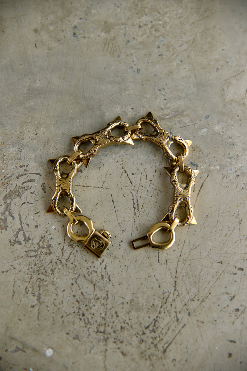A vintage gold-tone chain bracelet with star-shaped links and a lobster clasp, displayed on a textured, scratched gray surface.