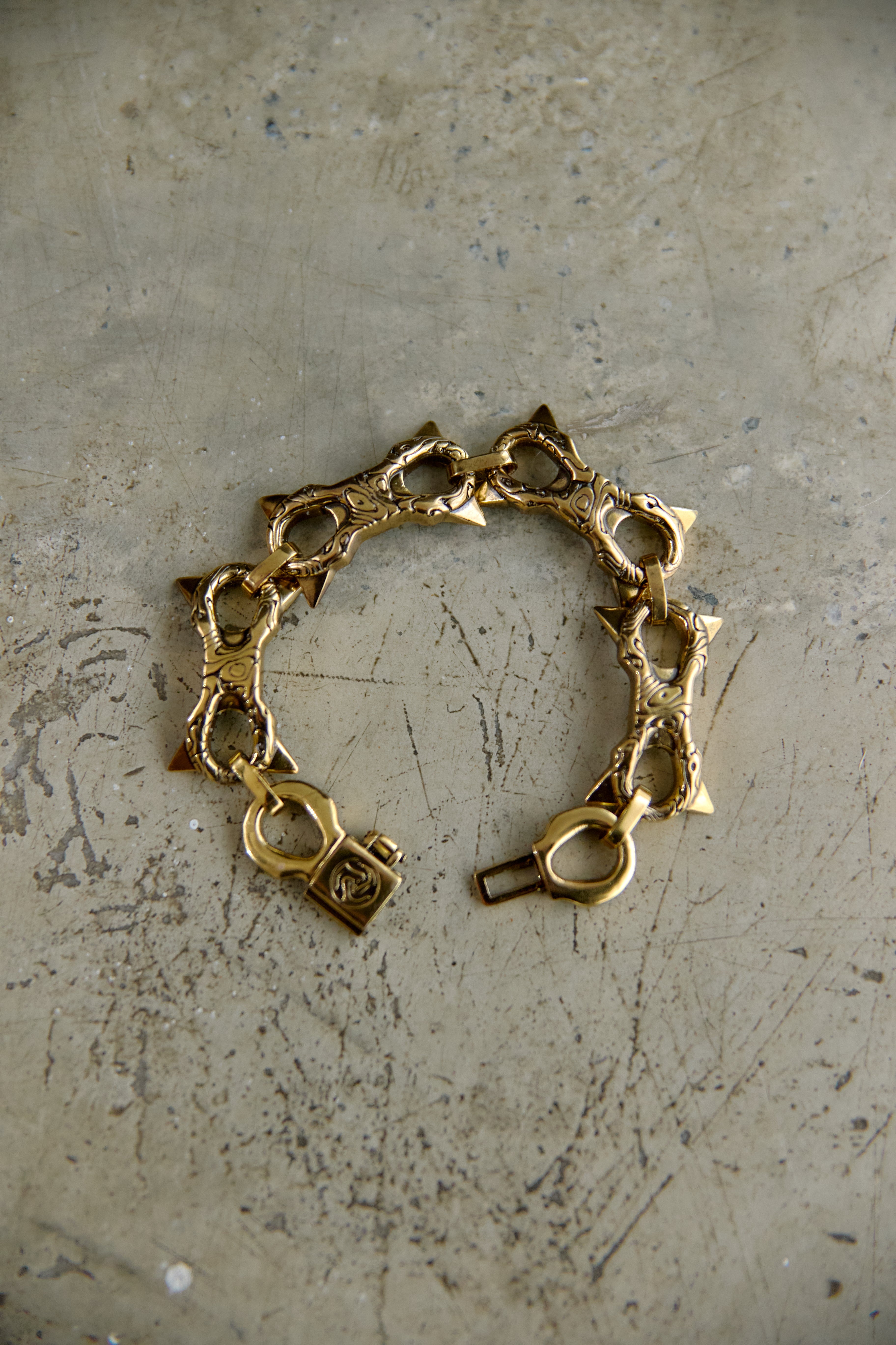 A vintage gold-tone chain bracelet with star-shaped links and a lobster clasp, displayed on a textured, scratched gray surface.