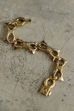A gold-tone chain bracelet with triangular spikes and a padlock charm, displayed on a textured gray surface.