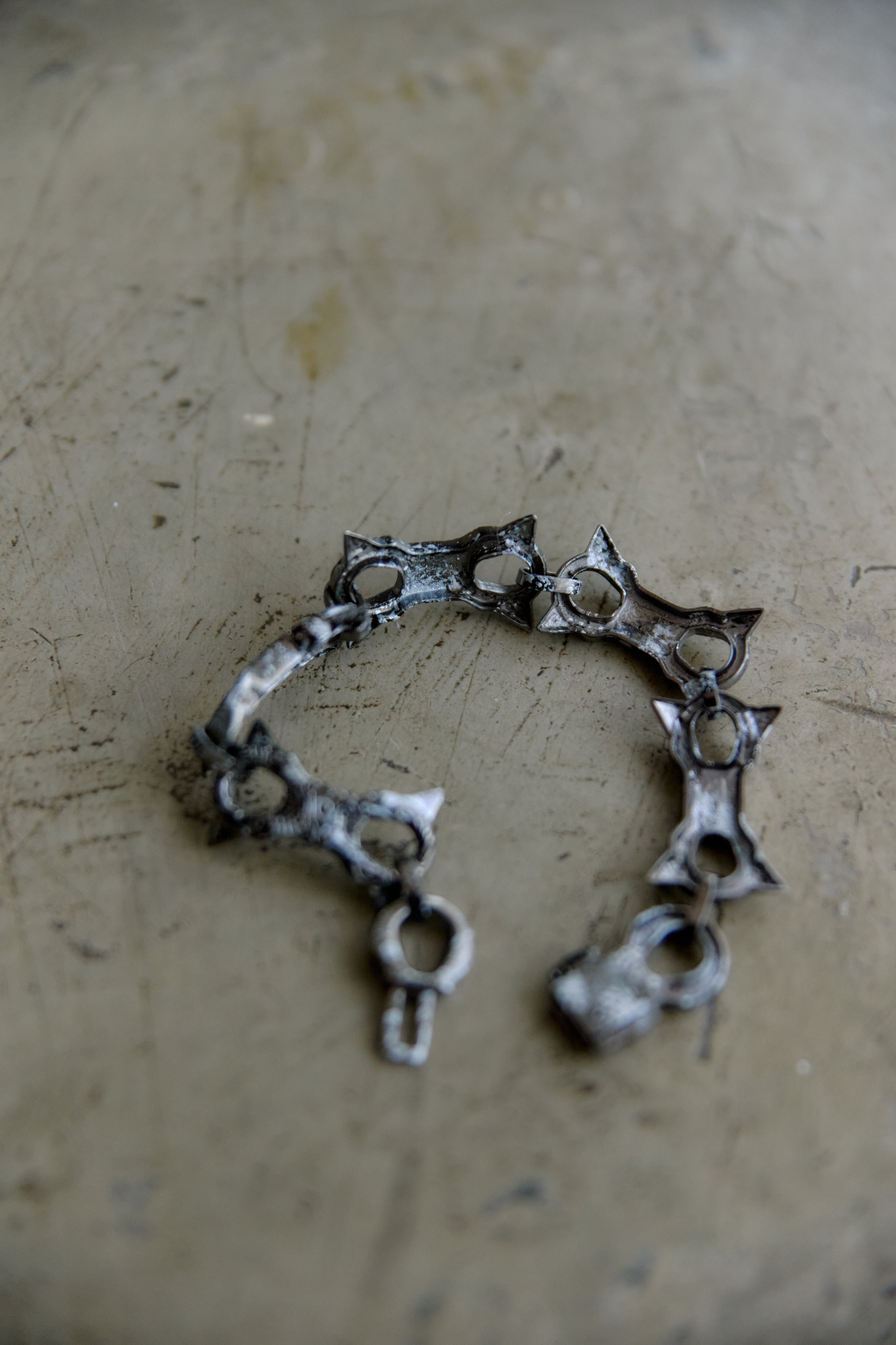 A handmade sterling silver cuff bracelet with star-shaped links and a lobster clasp, resting on a textured, scratched beige surface.