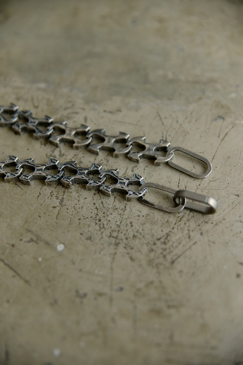 A close-up of a silver-toned metal chain with repeating star-shaped links and lobster clasp ends, laid on a textured beige surface.