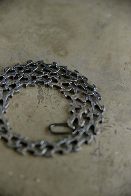 A coiled dark metallic chain with a small black spring clip, resting on a textured beige concrete surface.