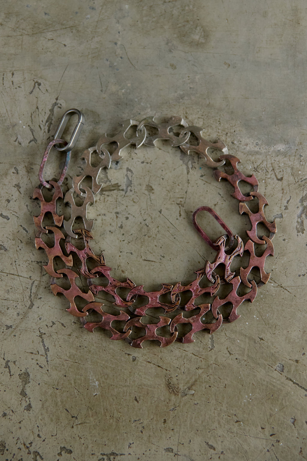 A bicycle chain guard with a reddish-brown protective plate and silver metal chain links, laid flat on a textured concrete surface.