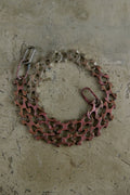 A bicycle chain guard with a reddish-brown protective plate and silver metal chain links, laid flat on a textured concrete surface.