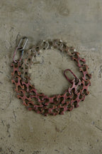 A bicycle chain guard with a reddish-brown protective plate and silver metal chain links, laid flat on a textured concrete surface.