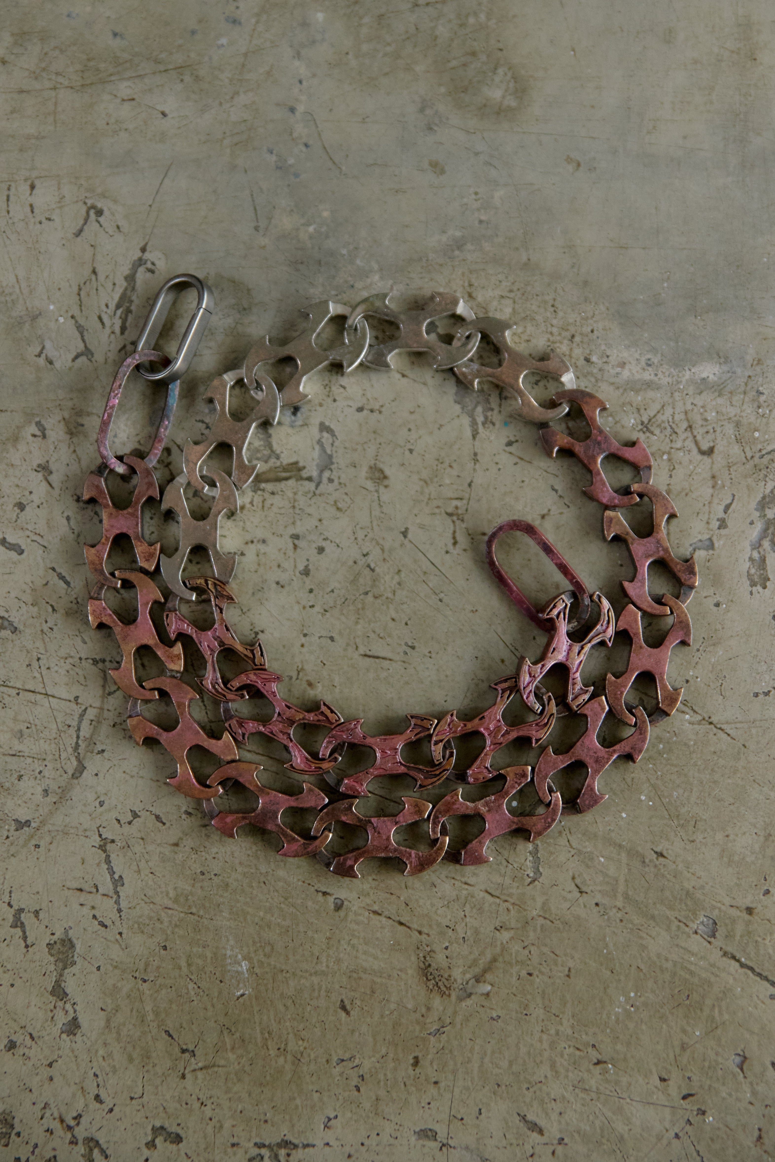 A bicycle chain guard with a reddish-brown protective plate and silver metal chain links, laid flat on a textured concrete surface.