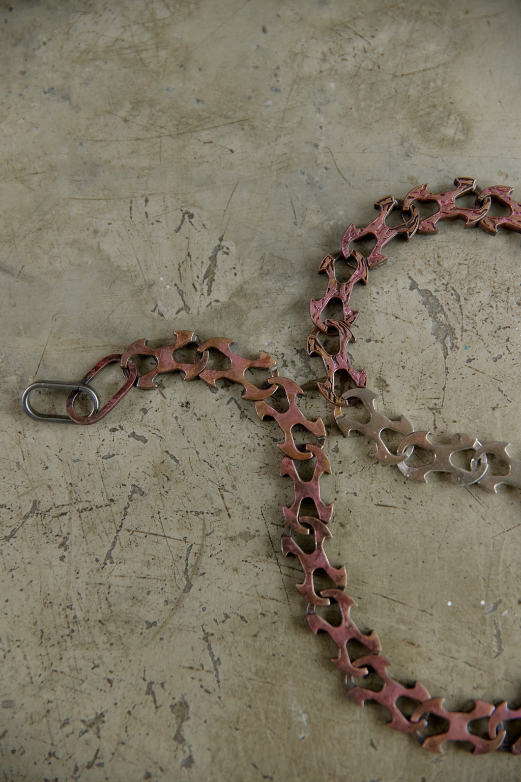 A rusted metal chain link with a silver spring ring clasp, lying on a textured concrete floor.