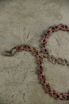 A rusted metal chain link with a silver spring ring clasp, lying on a textured concrete floor.