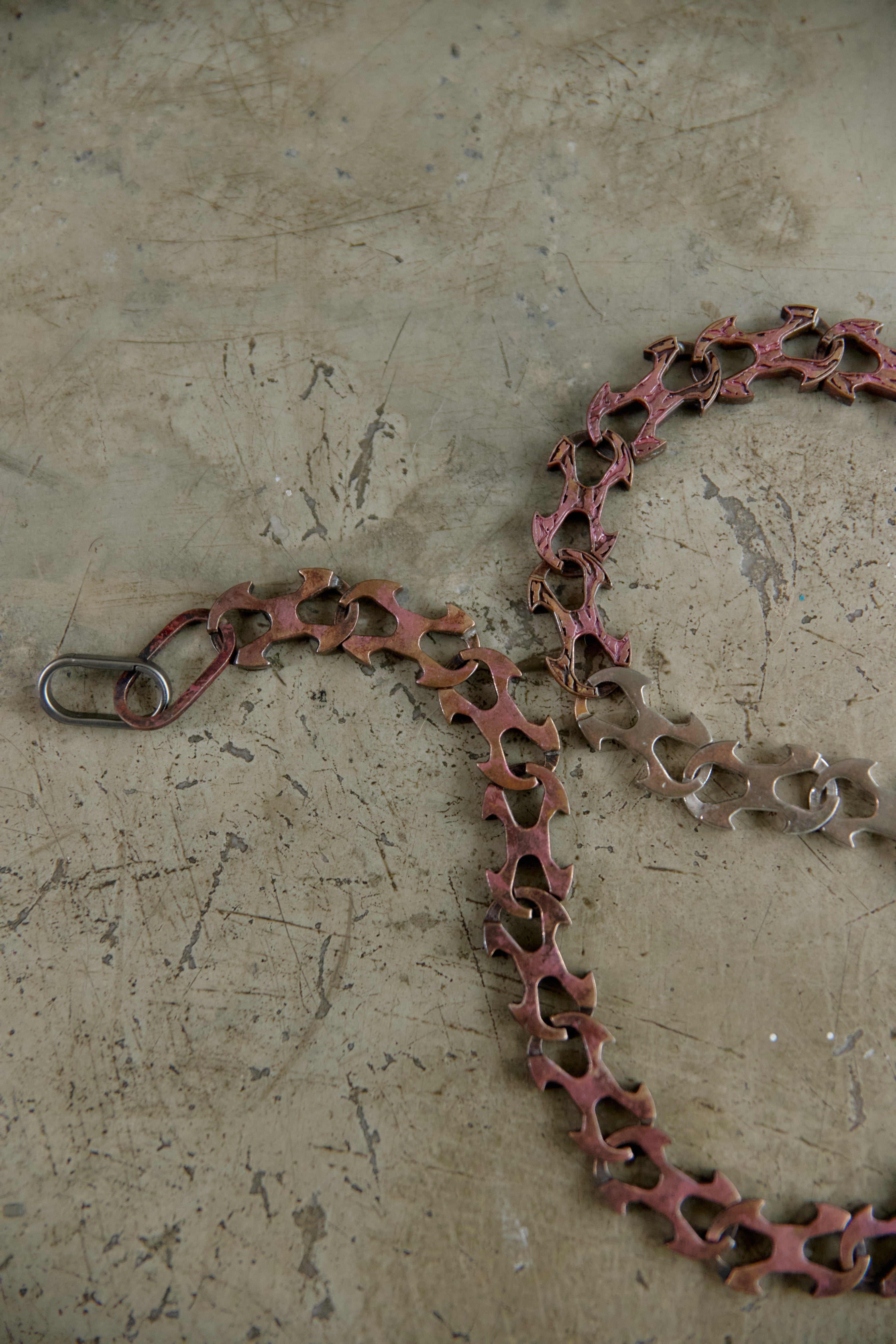 A rusted metal chain link with a silver spring ring clasp, lying on a textured concrete floor.