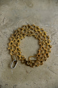 A coiled gold-tone bicycle chain link chain with a silver metal clasp, resting on a textured concrete surface.