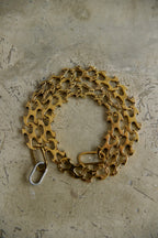 A coiled gold-tone bicycle chain link chain with a silver metal clasp, resting on a textured concrete surface.