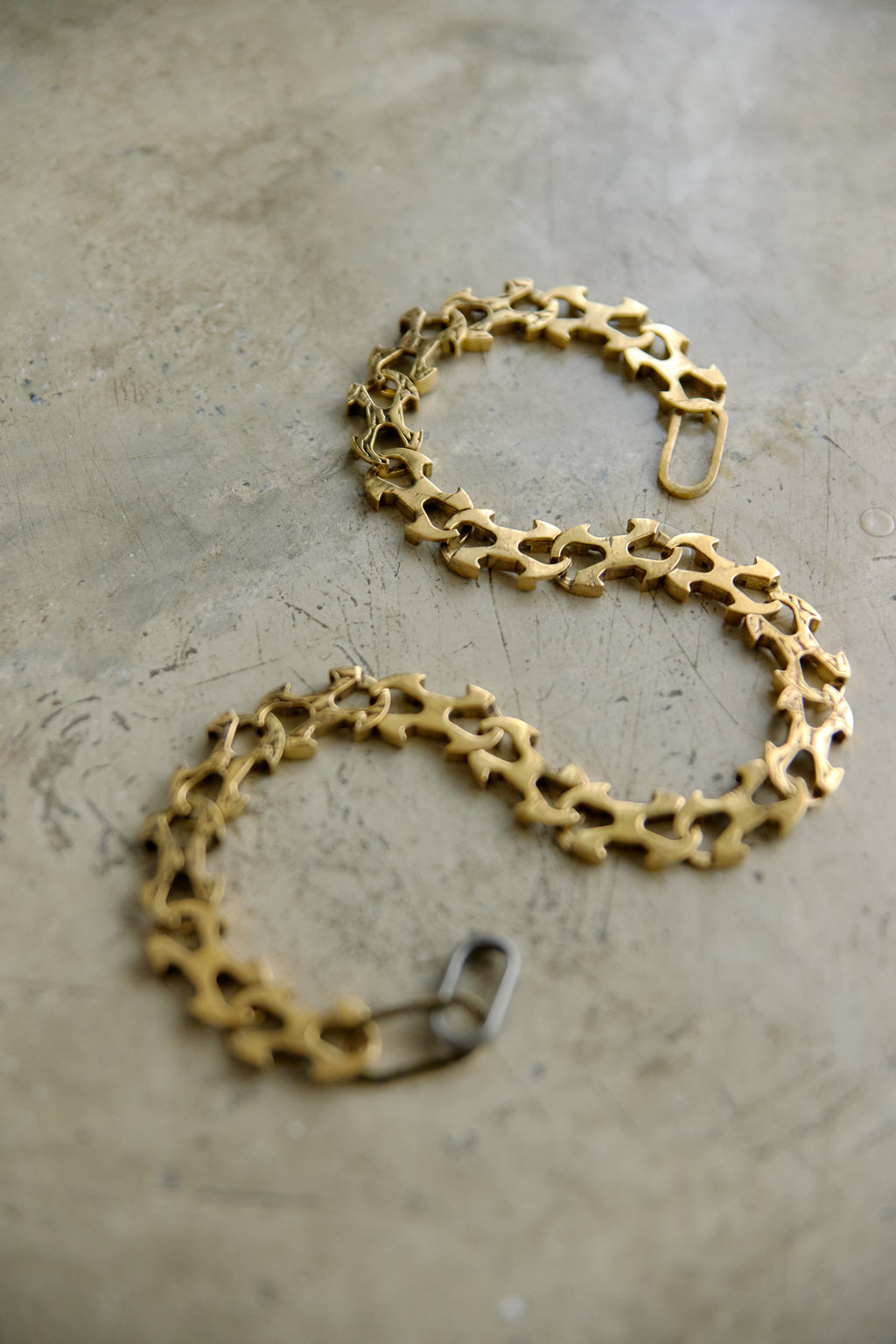 A gold-toned chain bracelet with a unique openwork, gear-like link design, displayed on a textured concrete surface.