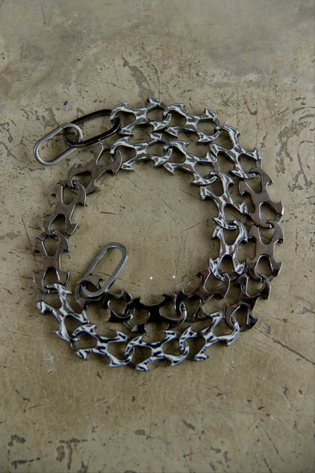 A bicycle chain guard made from recycled bicycle chains and metal parts, arranged in a circular shape on a textured concrete surface.