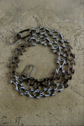 A bicycle chain guard made from recycled bicycle chains and metal parts, arranged in a circular shape on a textured concrete surface.
