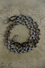 A bicycle chain guard made from recycled bicycle chains and metal parts, arranged in a circular shape on a textured concrete surface.