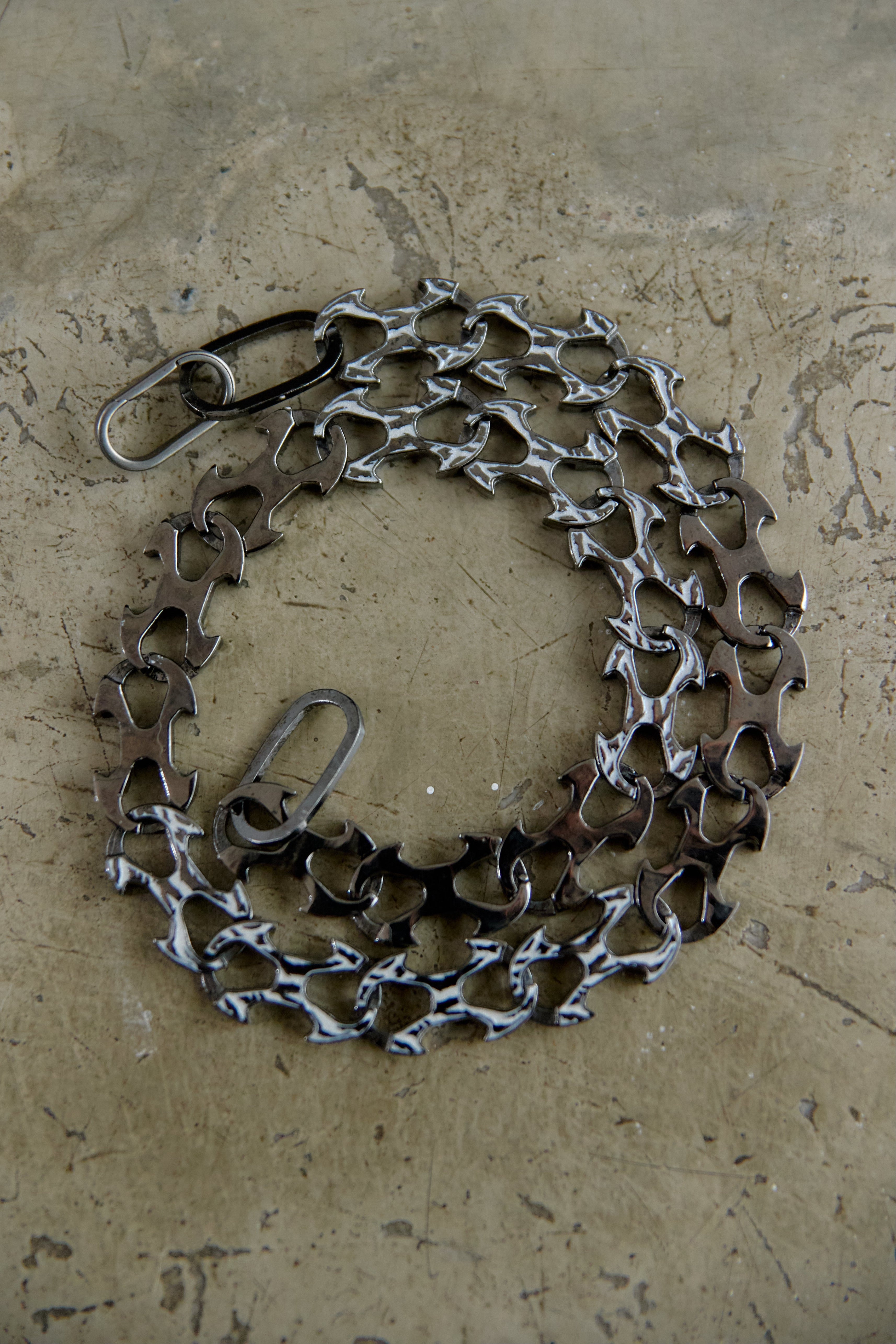 A bicycle chain guard made from recycled bicycle chains and metal parts, arranged in a circular shape on a textured concrete surface.