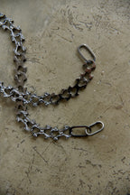 A handmade metal chain accessory with a unique textured, hammered finish, laid out on a textured concrete surface.