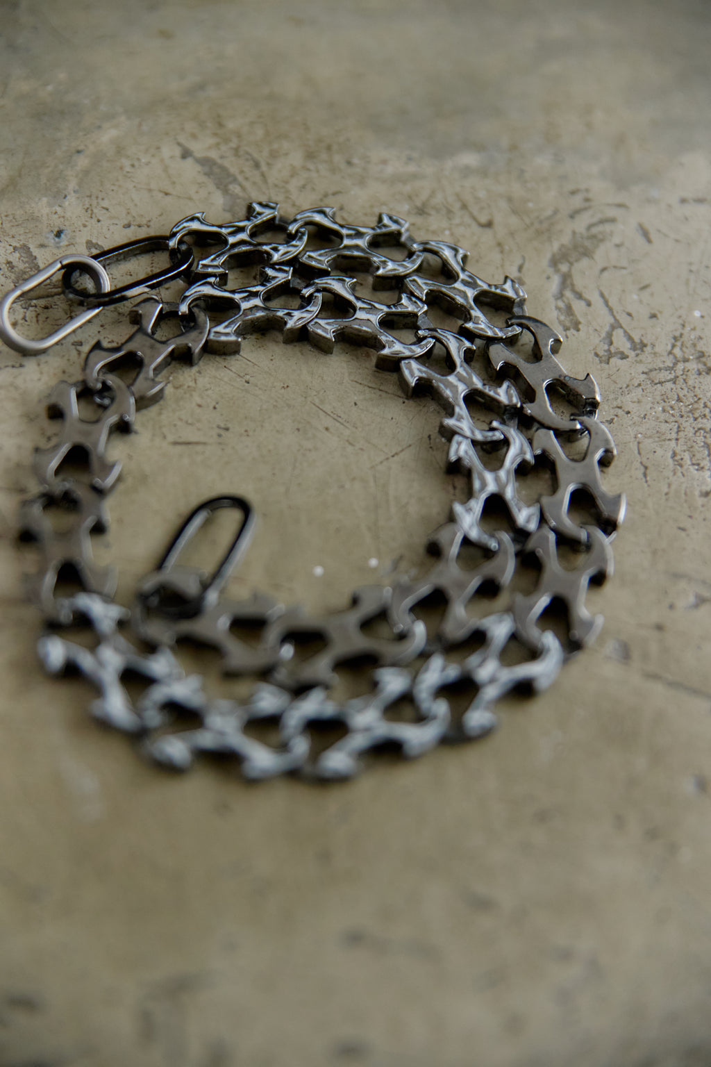 A bicycle cassette chain guard made from interlocking bicycle cassette sprockets, shown in a dark metallic finish on a textured concrete surface.