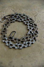A bicycle cassette chain guard made from interlocking bicycle cassette sprockets, shown in a dark metallic finish on a textured concrete surface.