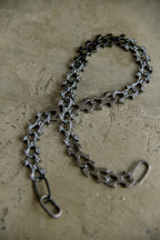 A dark metallic bicycle chain link chain with a matching rear hook, laid out on a textured concrete surface.