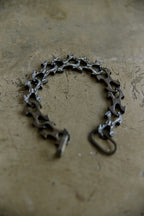 A bicycle chain-link style bracelet or necklace made from repurposed bicycle chain links, displayed on a textured concrete surface.