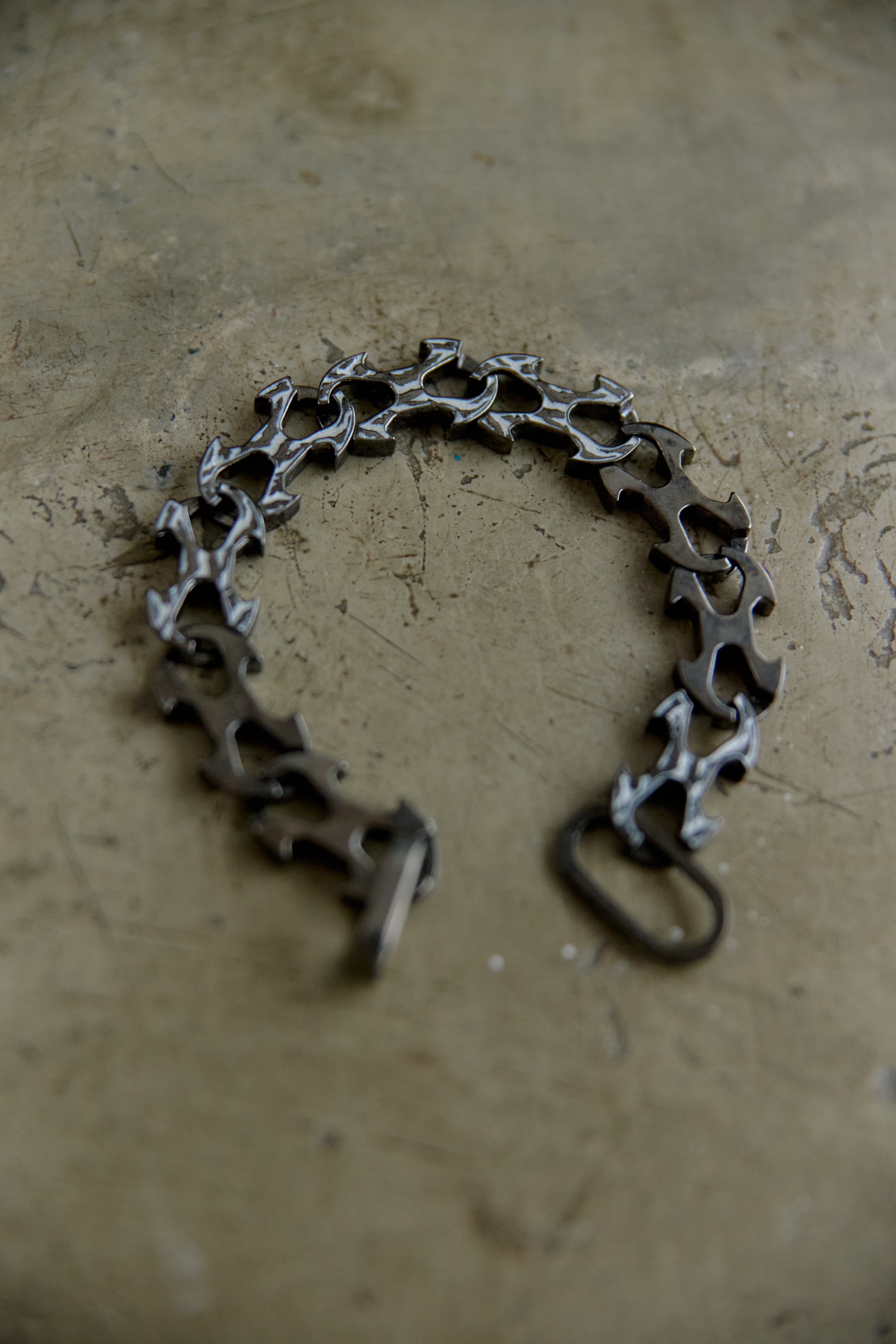 A bicycle chain-link style bracelet or necklace made from repurposed bicycle chain links, displayed on a textured concrete surface.