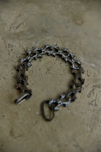 A dark metallic link bracelet with a unique star-shaped cutout design, displayed on a textured concrete surface.