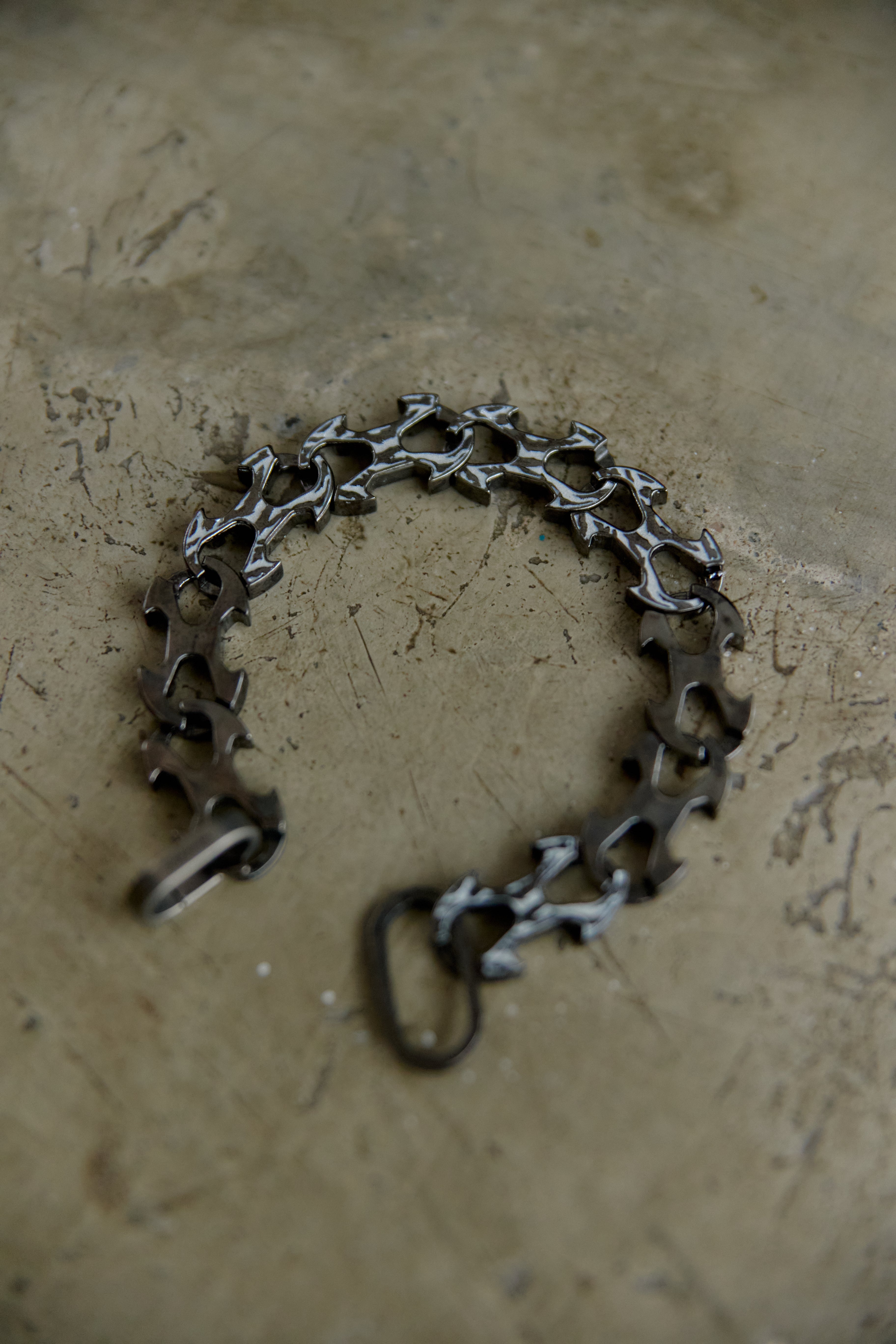 A dark metallic link bracelet with a unique star-shaped cutout design, displayed on a textured concrete surface.