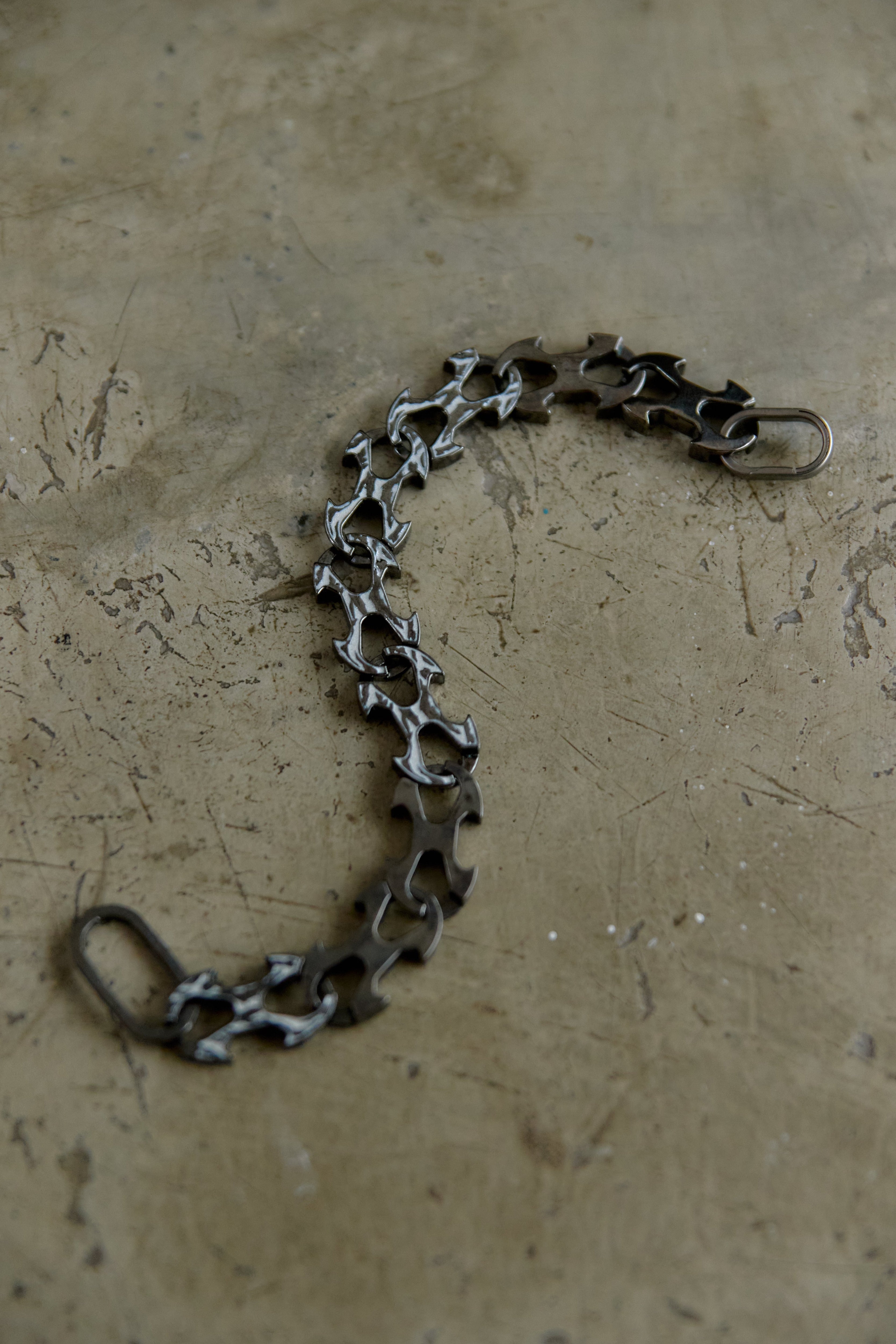 A dark metallic chain link accessory with a lobster clasp, laid out on a textured beige surface.