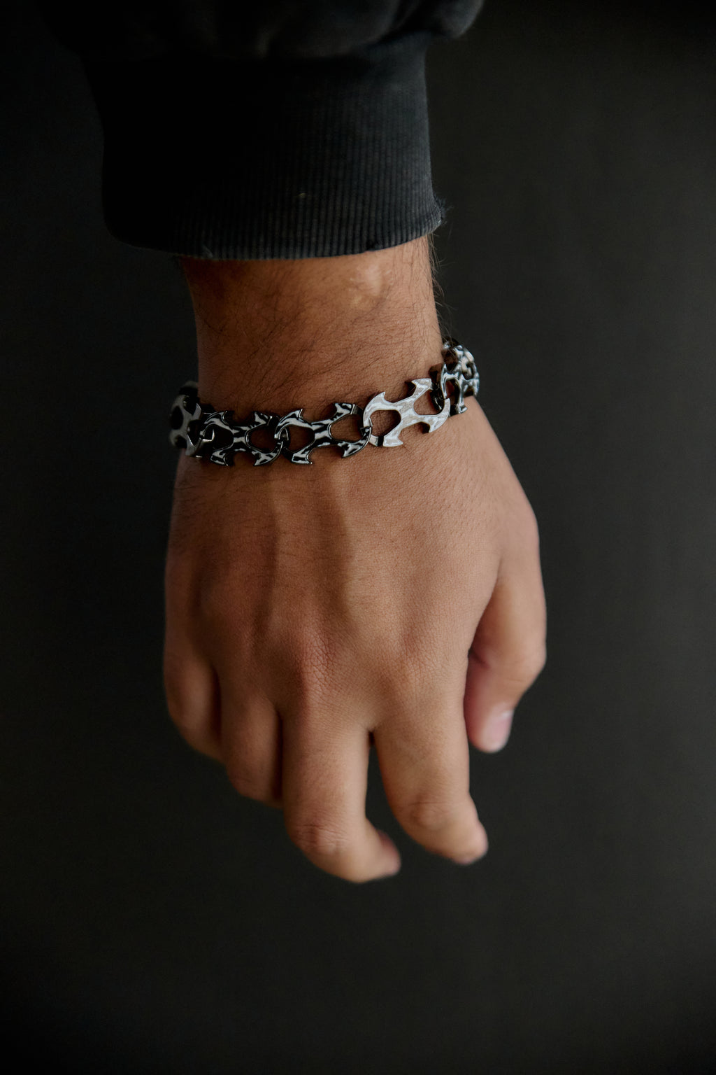 A close-up of a person's wrist wearing a silver chain bracelet with black and white abstract patterns, set against a dark background.