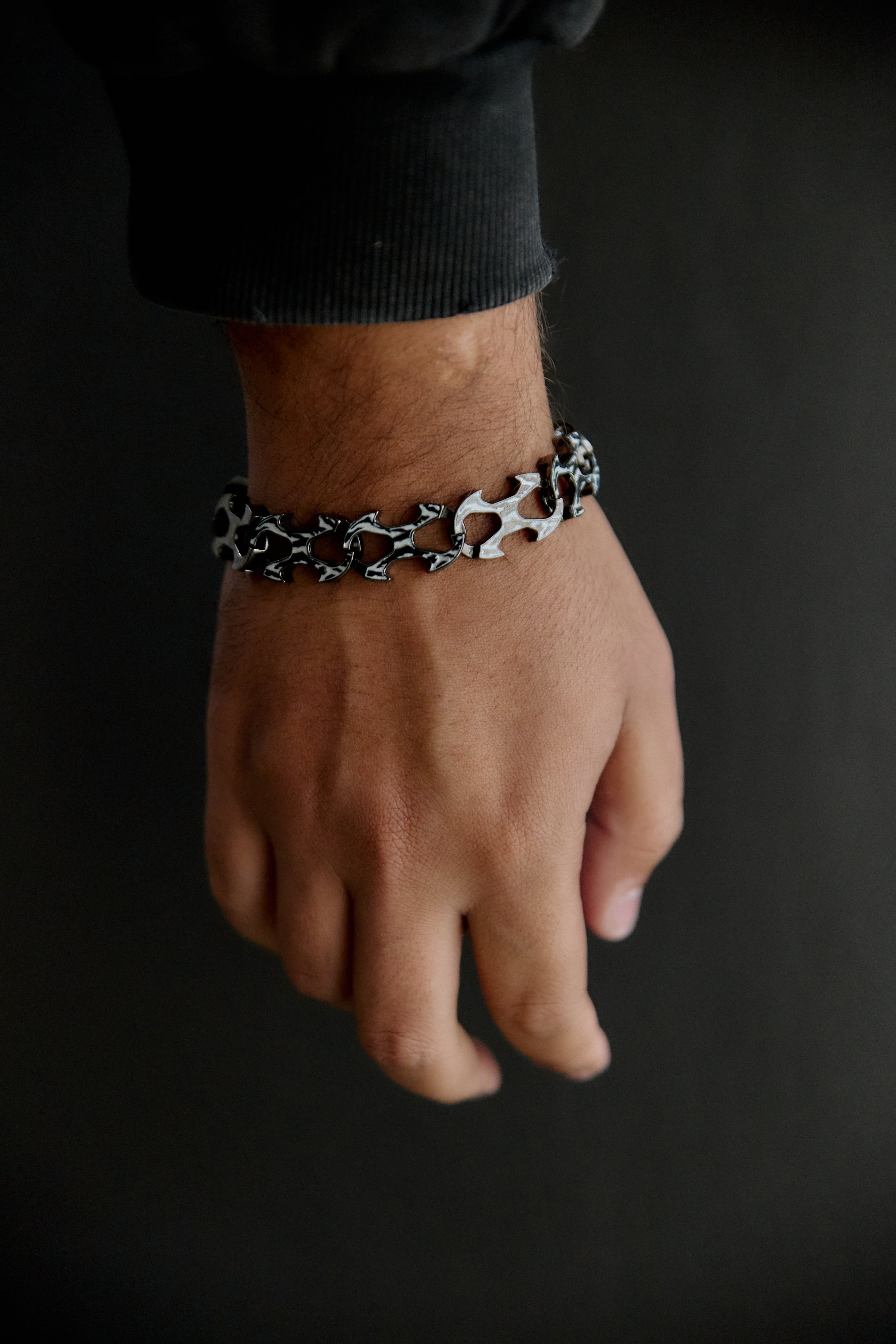 A close-up of a person's wrist wearing a silver chain bracelet with black and white abstract patterns, set against a dark background.