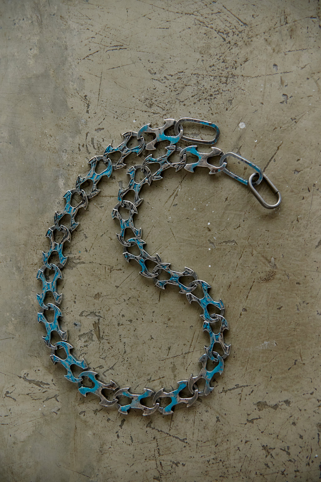 A bicycle chain link chain with turquoise blue paint accents on the links, coiled on a textured concrete surface.