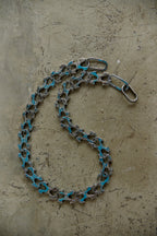 A bicycle chain link chain with turquoise blue paint accents on the links, coiled on a textured concrete surface.