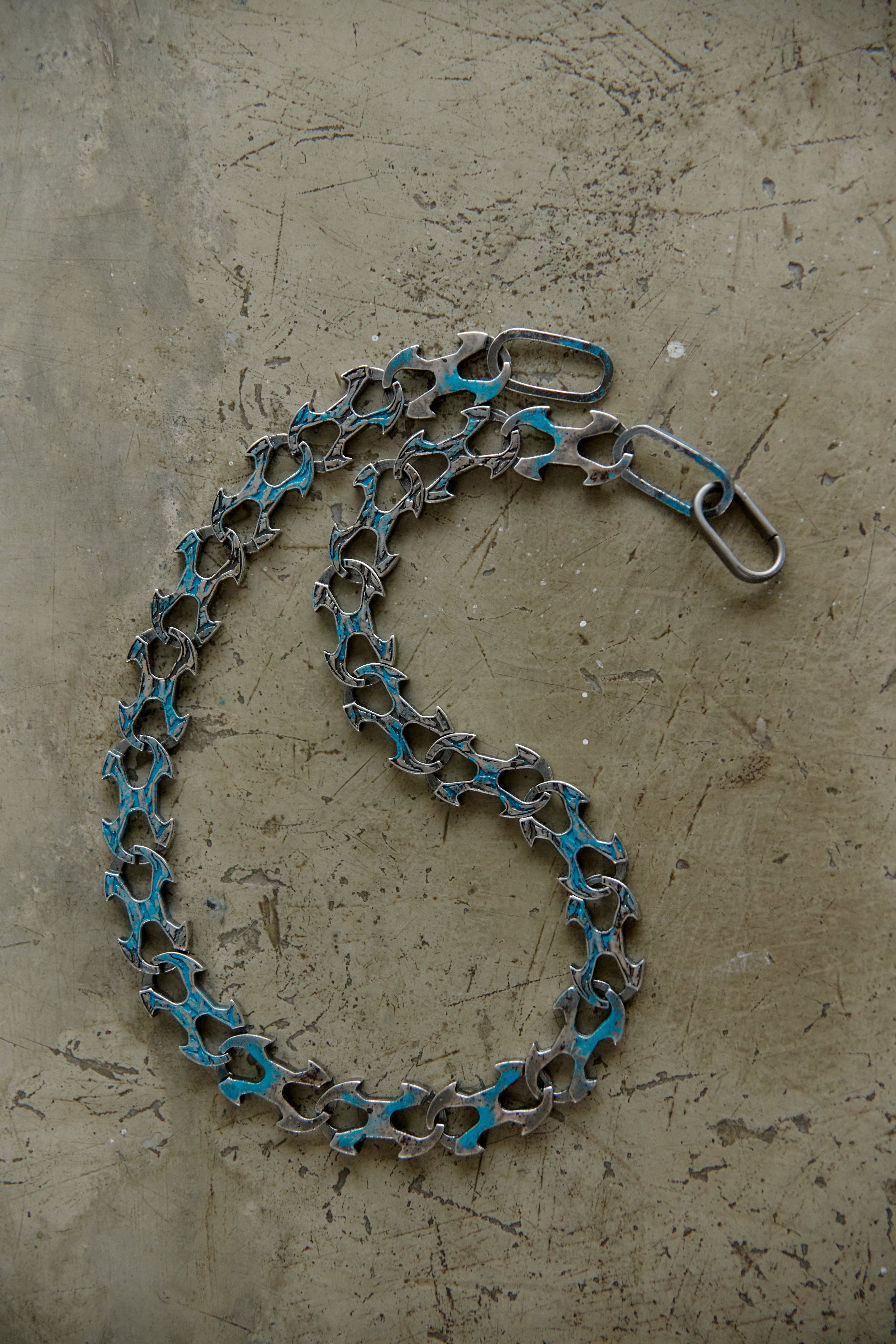 A bicycle chain link chain with turquoise blue paint accents on the links, coiled on a textured concrete surface.