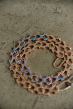 A copper-colored bicycle chain guard or chain guard cover with a cutout pattern, laid flat on a textured gray surface.
