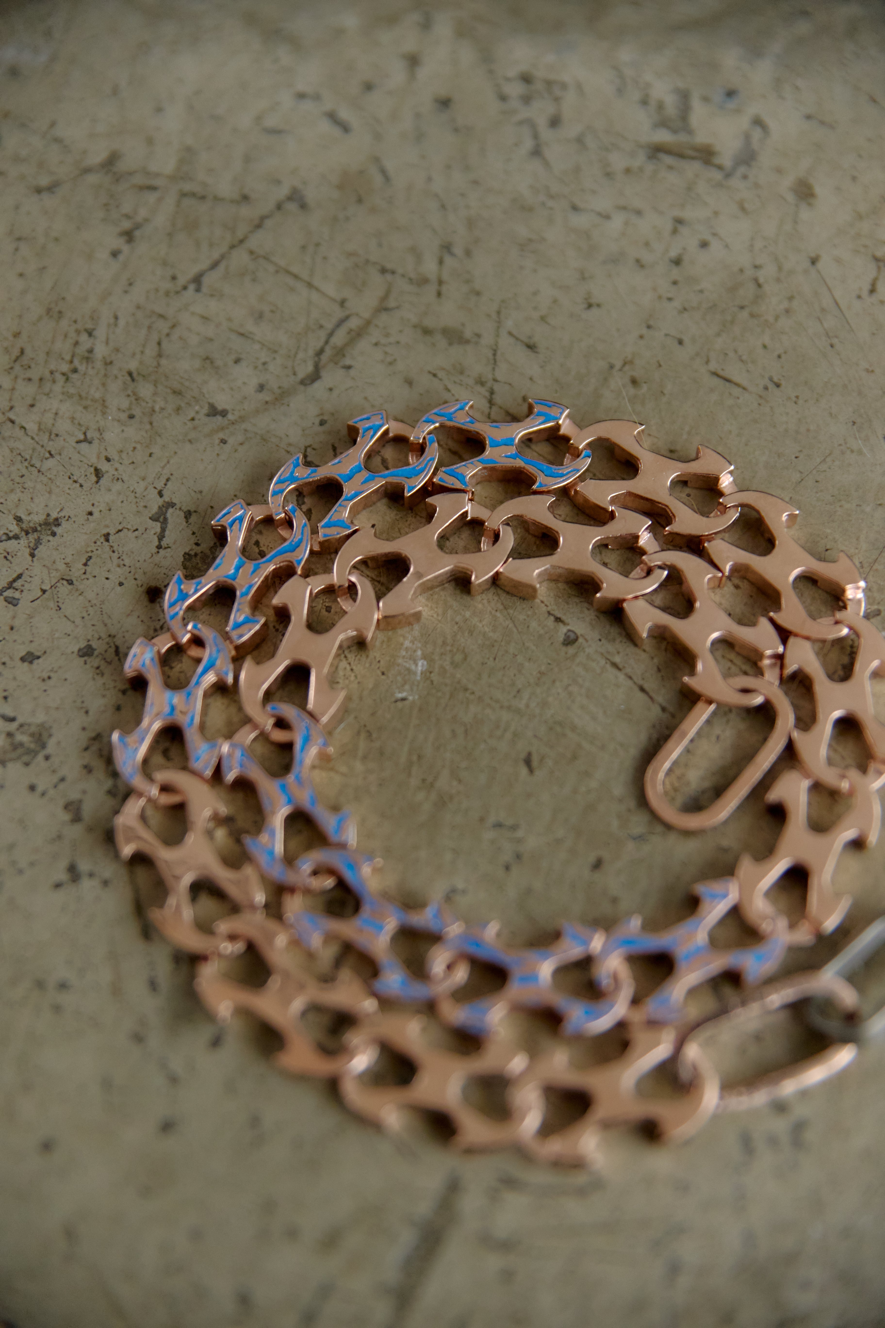 A copper-colored bicycle chain guard or chain guard cover with a cutout pattern, laid flat on a textured gray surface.