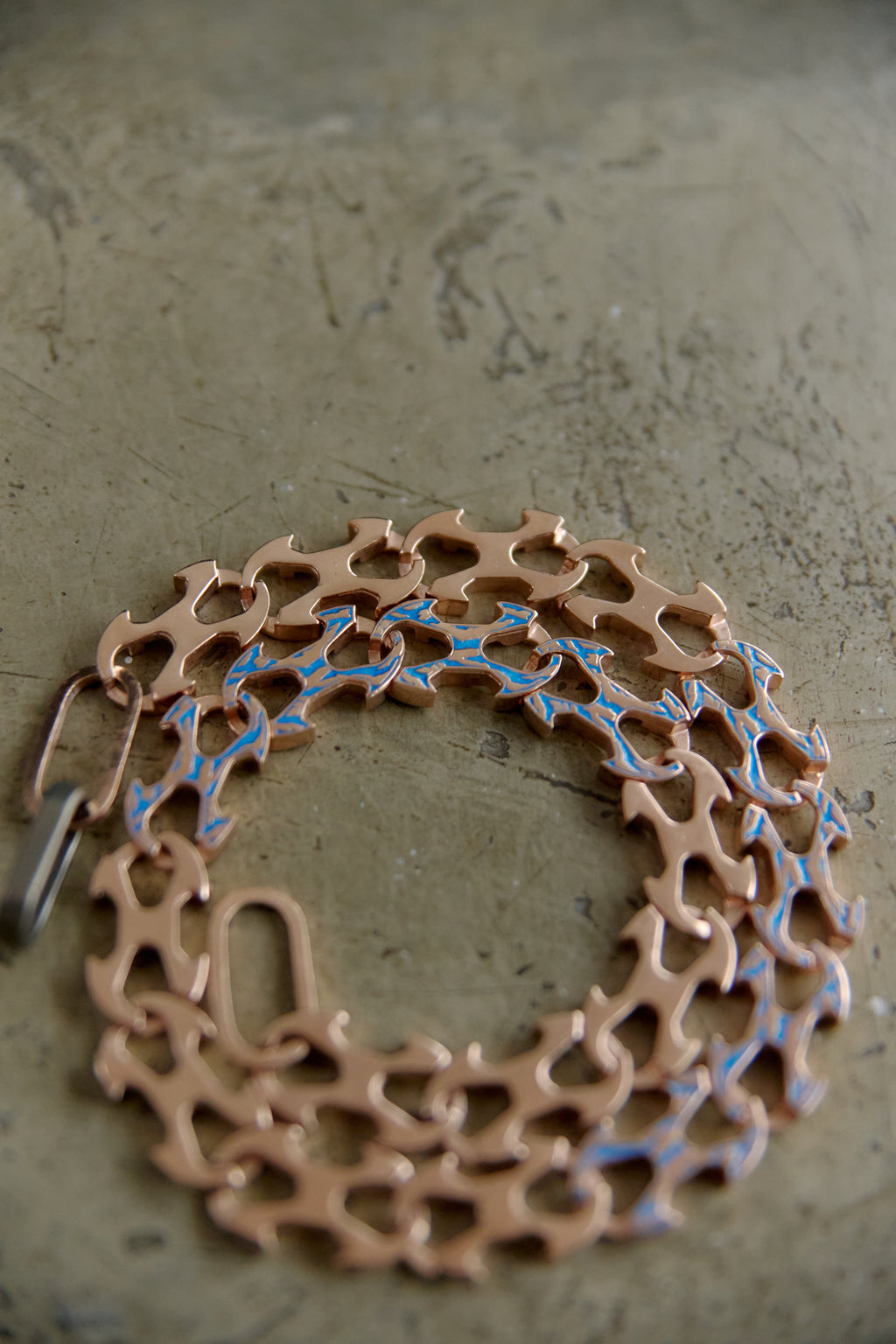 A copper-colored metal link chain bracelet with blue enamel accents, displayed on a textured gray surface.