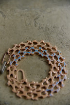 A copper-colored metal link chain bracelet with blue enamel accents, displayed on a textured gray surface.