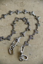 A graphite-toned metal chain necklace with textured, snake-like links and lobster clasps, displayed on a textured beige surface.